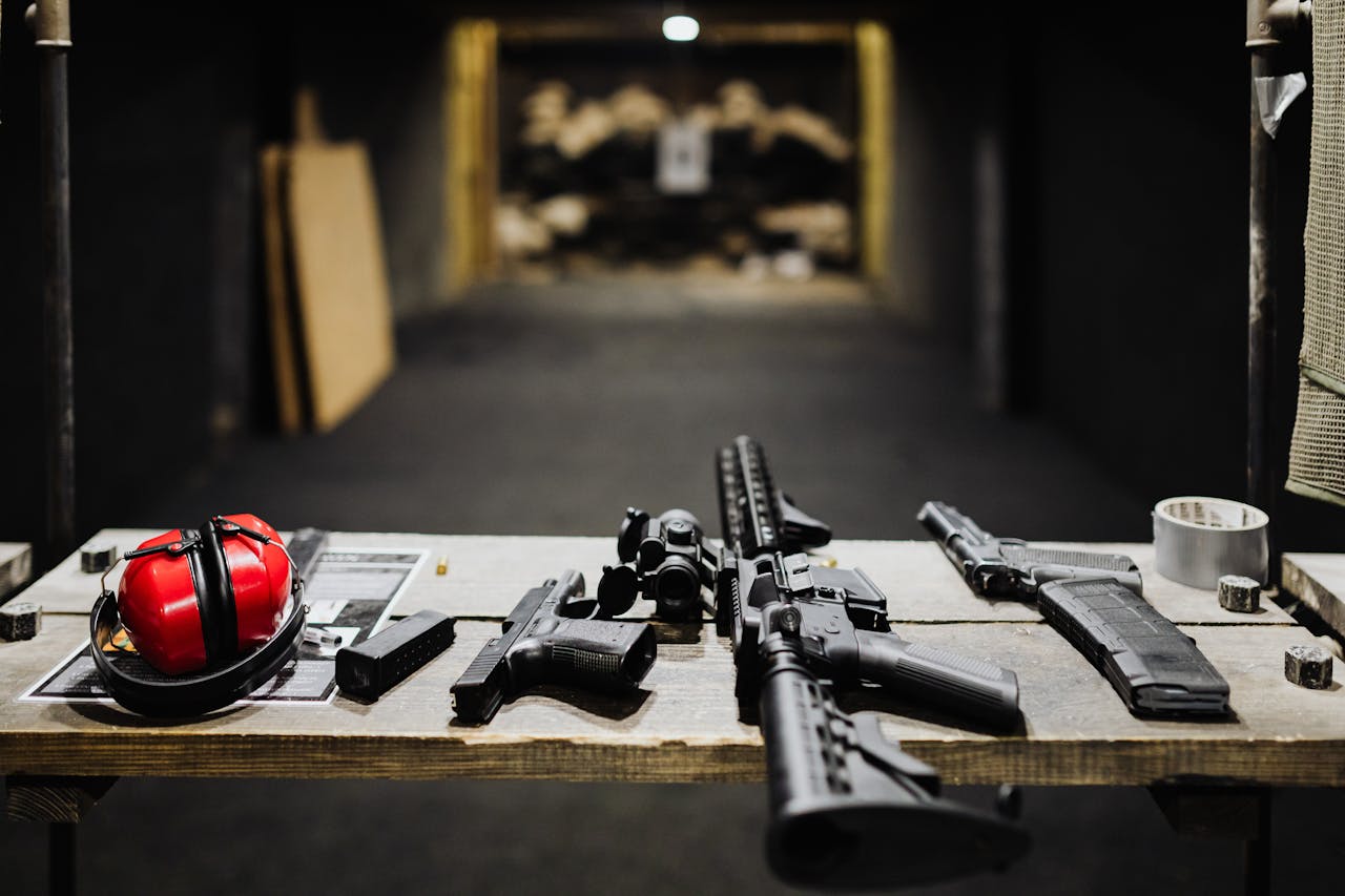 A selection of firearms and safety gear on a table at an indoor shooting range.